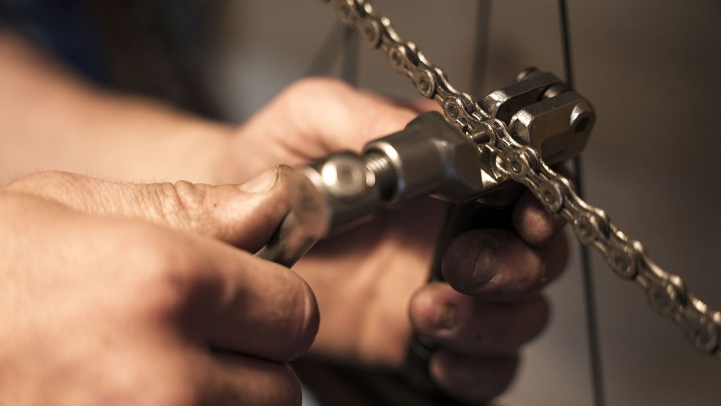 Man using a chain breaker to remove a bike chain from a bike