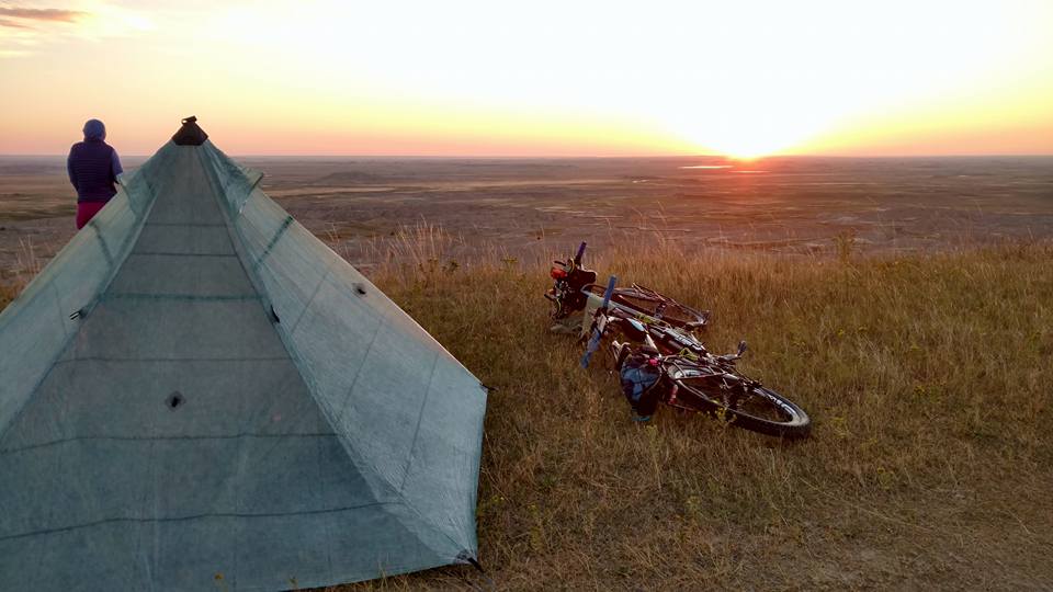 A touring cyclist watches the sunset from his tent and bike